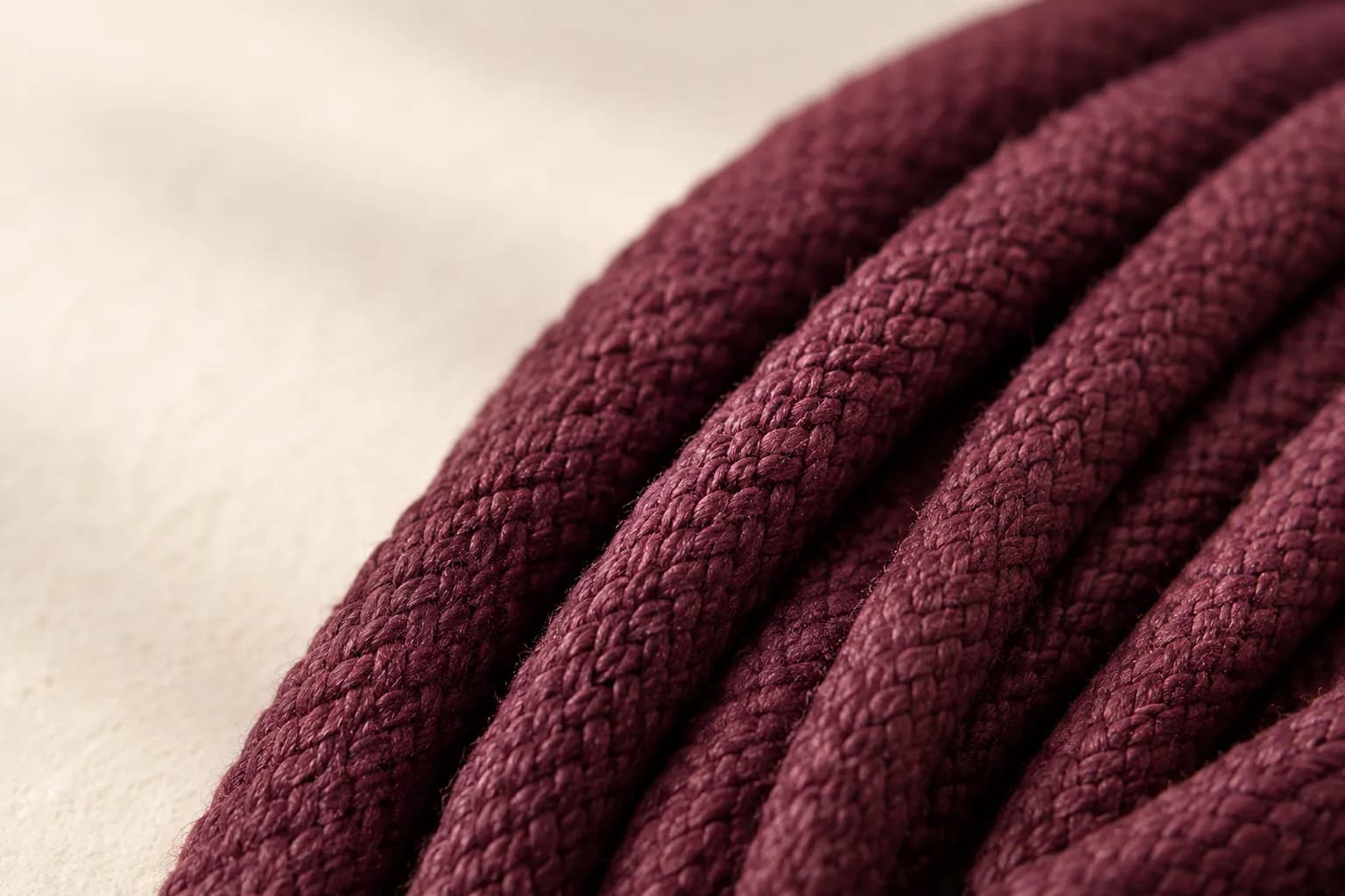 Close-up of several braided bordeaux cords side by side, with soft side light across the braid.
