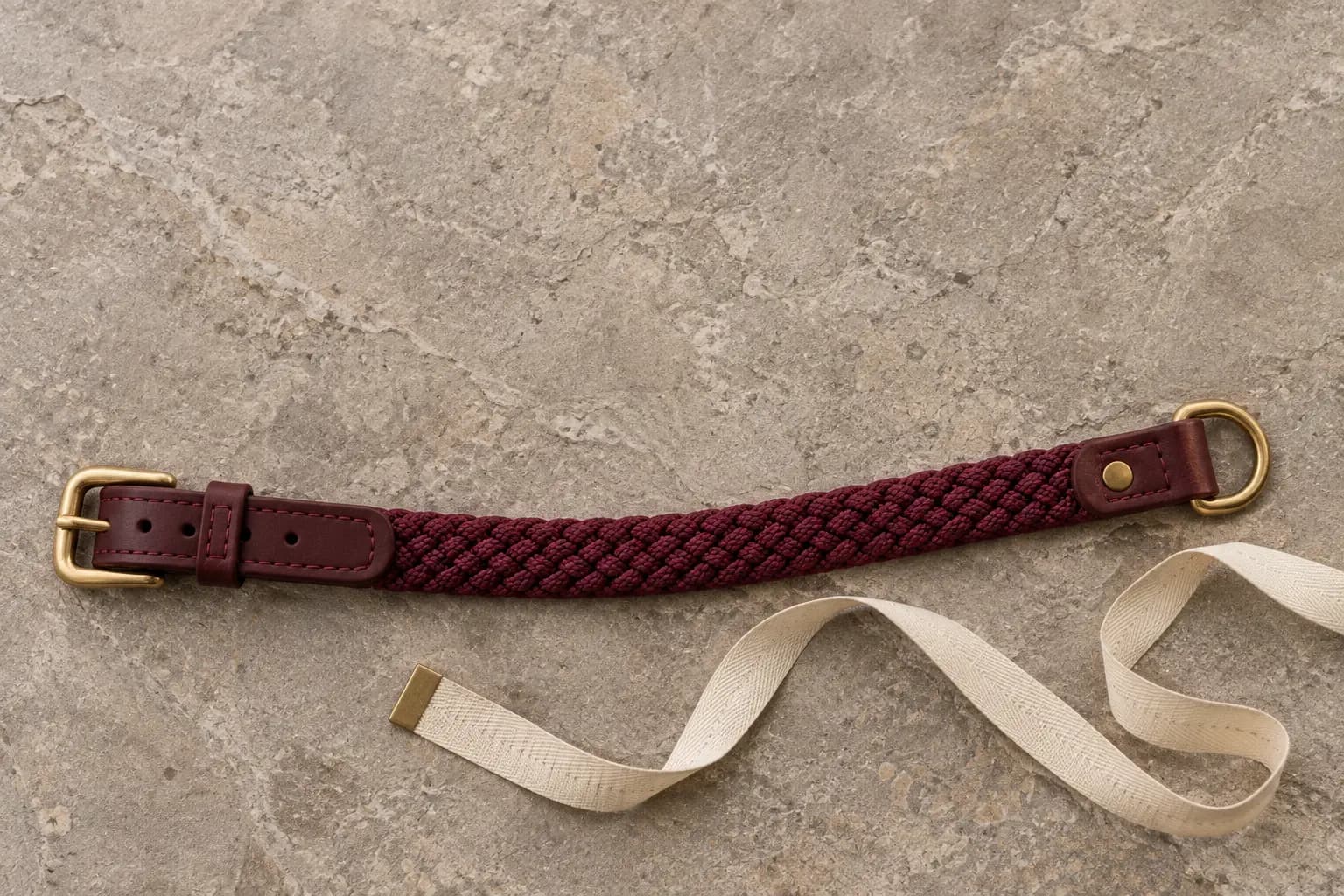 Halsband met gevlochten koord en leren gespband naast een meetlint, op een natuurstenen ondergrond.